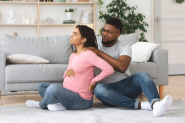 Pregnant black woman suffering from backache, husband massaging her shoulders.